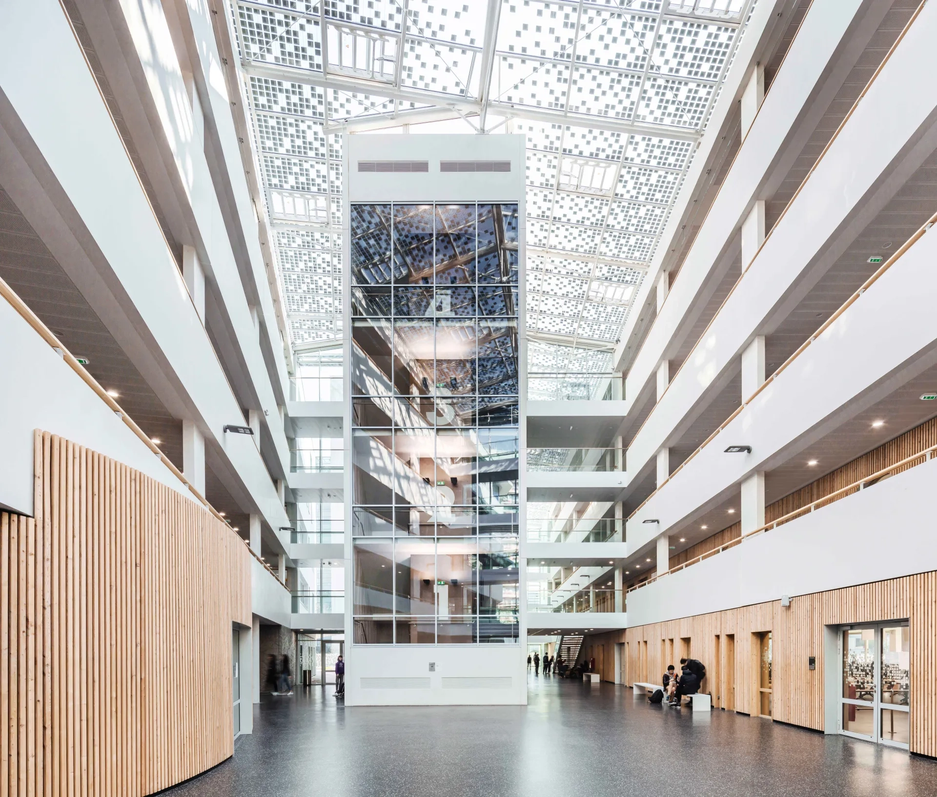 Les lignes  en béton poli blanc des coursives et les parois revêtues d’un bardage bois thermo-acoustique participent à l’ambiance accueillante  et chaleureuse de l’atrium.