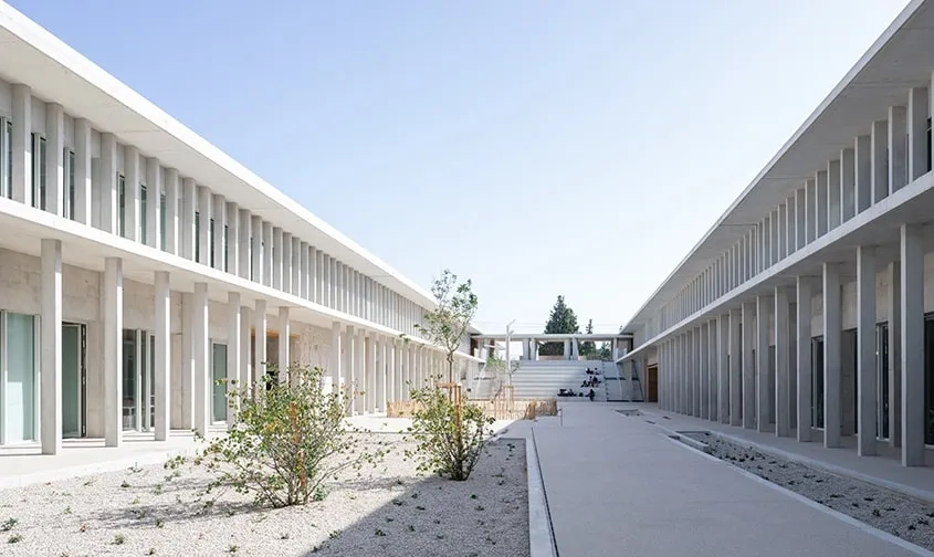 À l’image d’un cloître réinventé, les hauts portiques de béton du rez-de-chaussée protègent les circulations extérieures qui innervent l’ensemble du lycée.