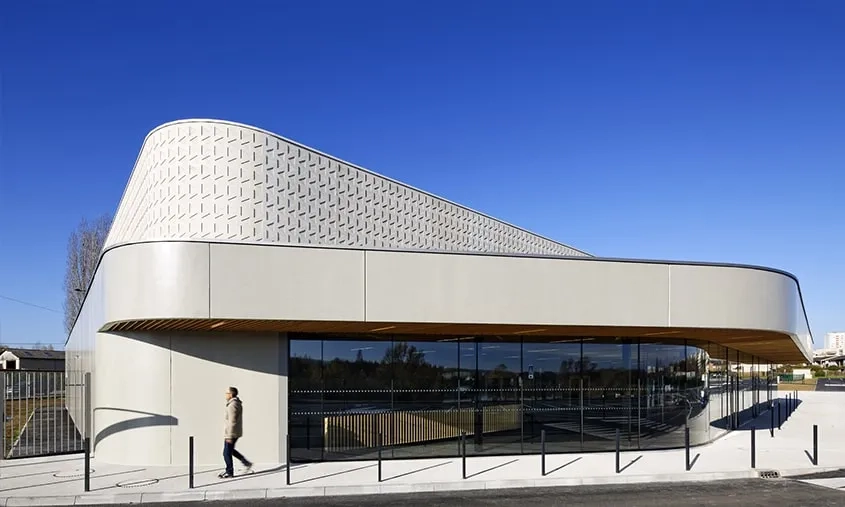 Le volume de la salle, visible en façades, est en béton gris très clair et présente un parement matricé. Au rez-de-chaussée, les façades sont réalisées avec des éléments préfabriqués en usine de type murs à coffrage intégré. © Franck DELETANG Le volume de la salle, visible en façades, est en béton gris très clair et présente un parement matricé. Au rez-de-chaussée, les façades sont réalisées avec des éléments préfabriqués en usine de type murs à coffrage intégré.