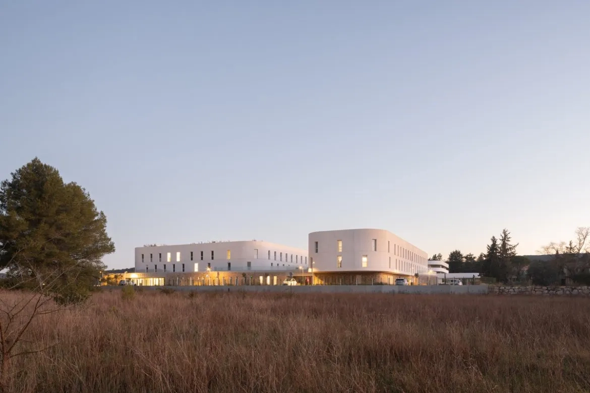 Vus de loin, les volumes supérieurs de béton blanc paraissent flotter au-dessus de leur socle en moellons qui, à l’inverse, semble bien ancré dans le terrain.